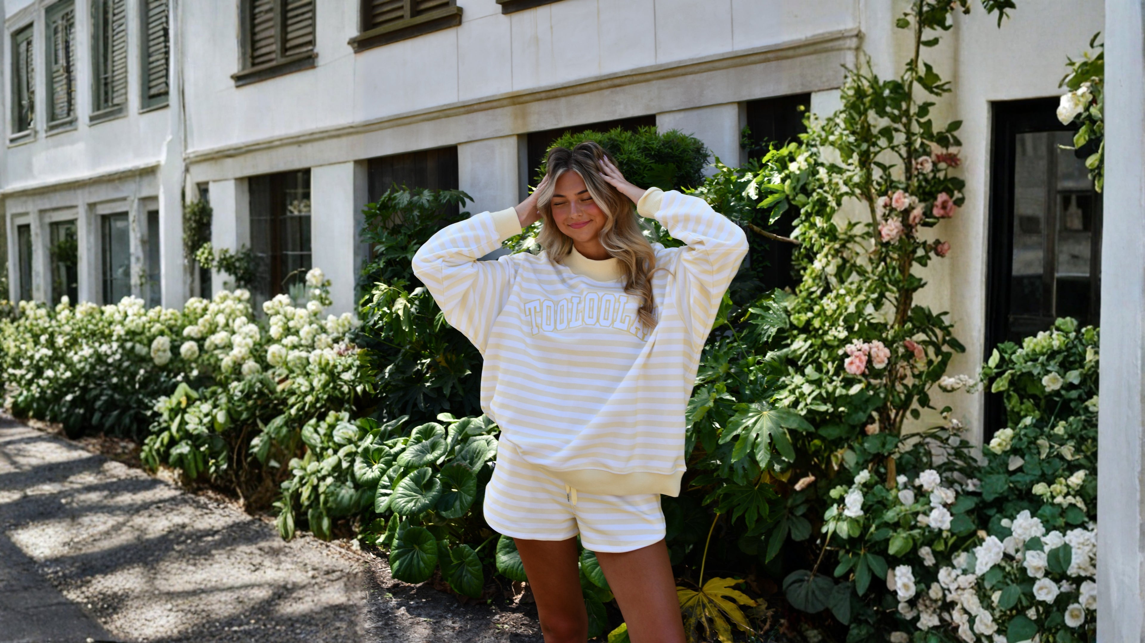 Woman in a white and yellow outfit standing in front of a building with greenery